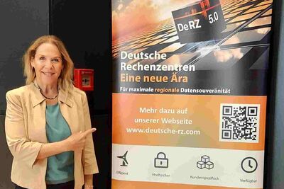 Susanne Back steht neben einem Werberollout der DeRZ mit Informaitonen &uuml;ber das Produkt DeRZ 5.0