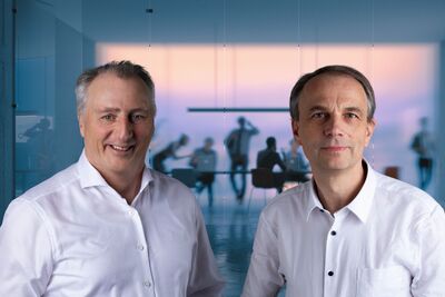 Stephan Sequens und Christoph Machner sowie im Hintergrund eine Teambesprechung